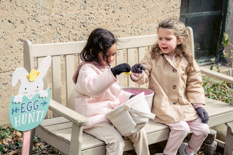 Cute Diverse Girls Playing With Easter Eggs On Garden Bench