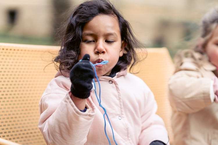 Content Ethnic Girl Blowing Bubbles On Bench In Spring Park