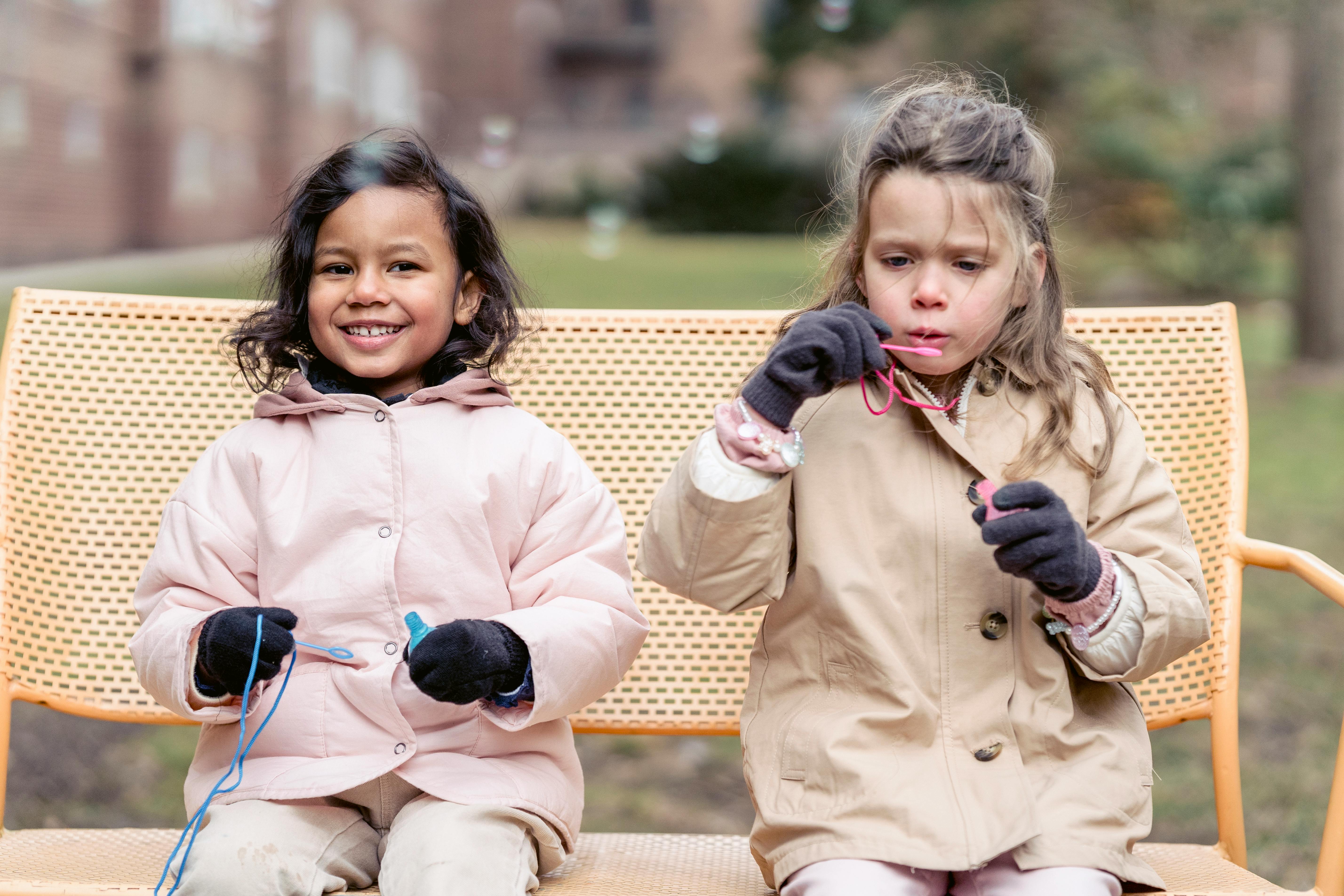 joyful multiethnic girls playing with soap bubbles in spring park