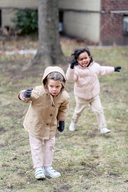 Full body joyful multiracial girls in warm clothes grimacing and having fun in spring park