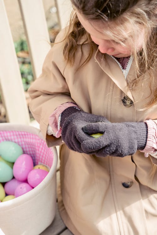 Crop girl on bench with decorative Easter eggs outdoors