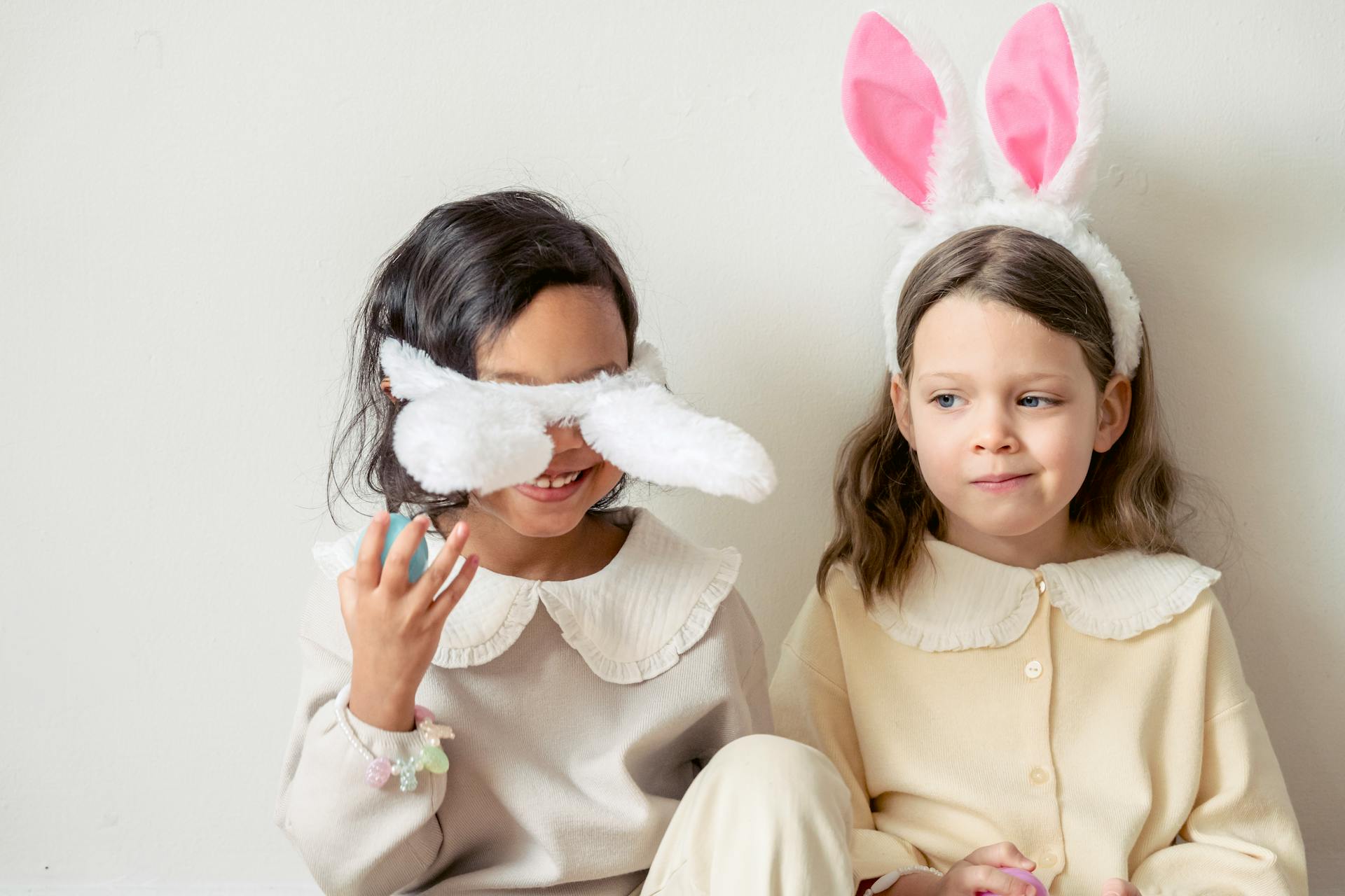 Smiling multiethnic girls playing with bunny ears on light background