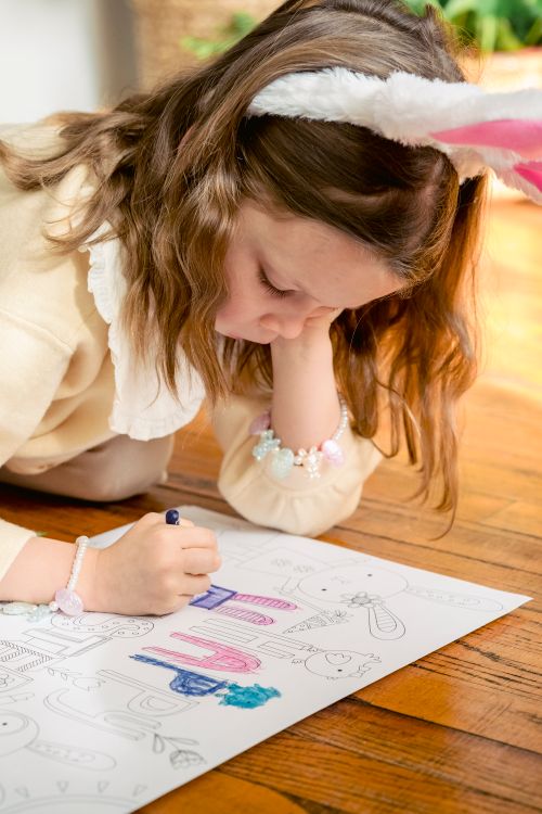 Free Preschool child with bunny ears leaning on hand while coloring paper drawing on parquet during festive occasion in house Stock Photo