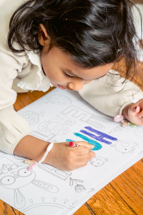 Free Crop Hispanic child coloring paper drawing with crayon while sitting on floor during festive event Stock Photo