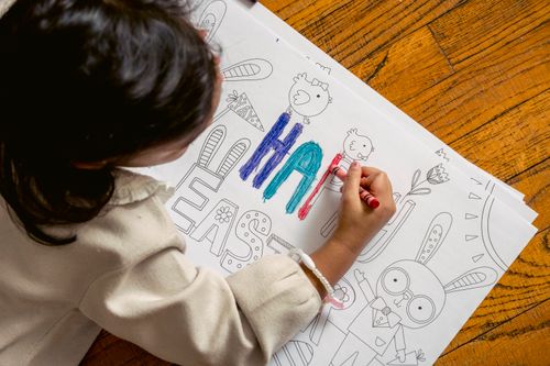 Free High angle back view of crop unrecognizable ethnic kid coloring Happy Easter inscription on drawing with crayon Stock Photo