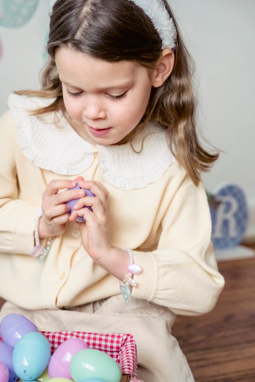 Free Crop gentle child with brown hair opening plastic egg on floor during festive event at home Stock Photo