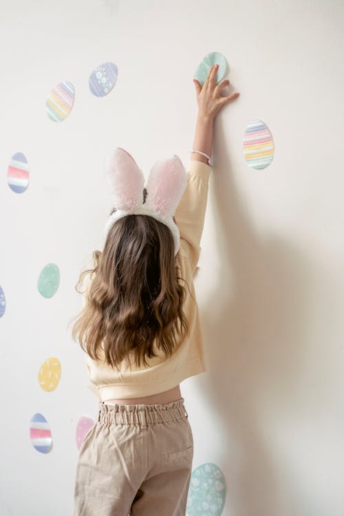 Unrecognizable girl decorating wall with paper eggs at home