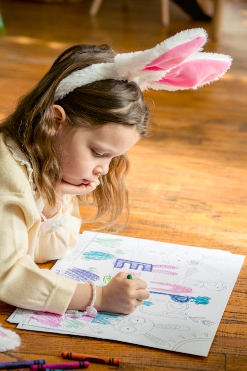 Free Charming girl with bunny ears coloring drawing on parquet Stock Photo