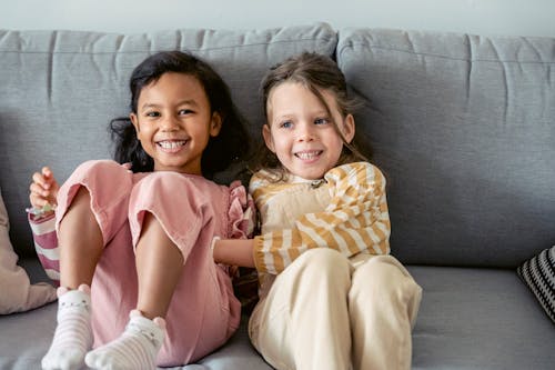 Cheerful best multiracial friends in striped clothes interacting on couch in living room in house