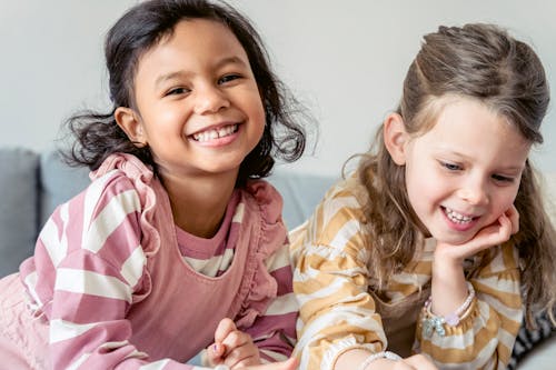 Smiling Hispanic child against sincere girlfriend in striped wear leaning on hand in house room