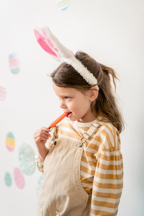 Charming girl with bunny ears eating carrot on Easter Day