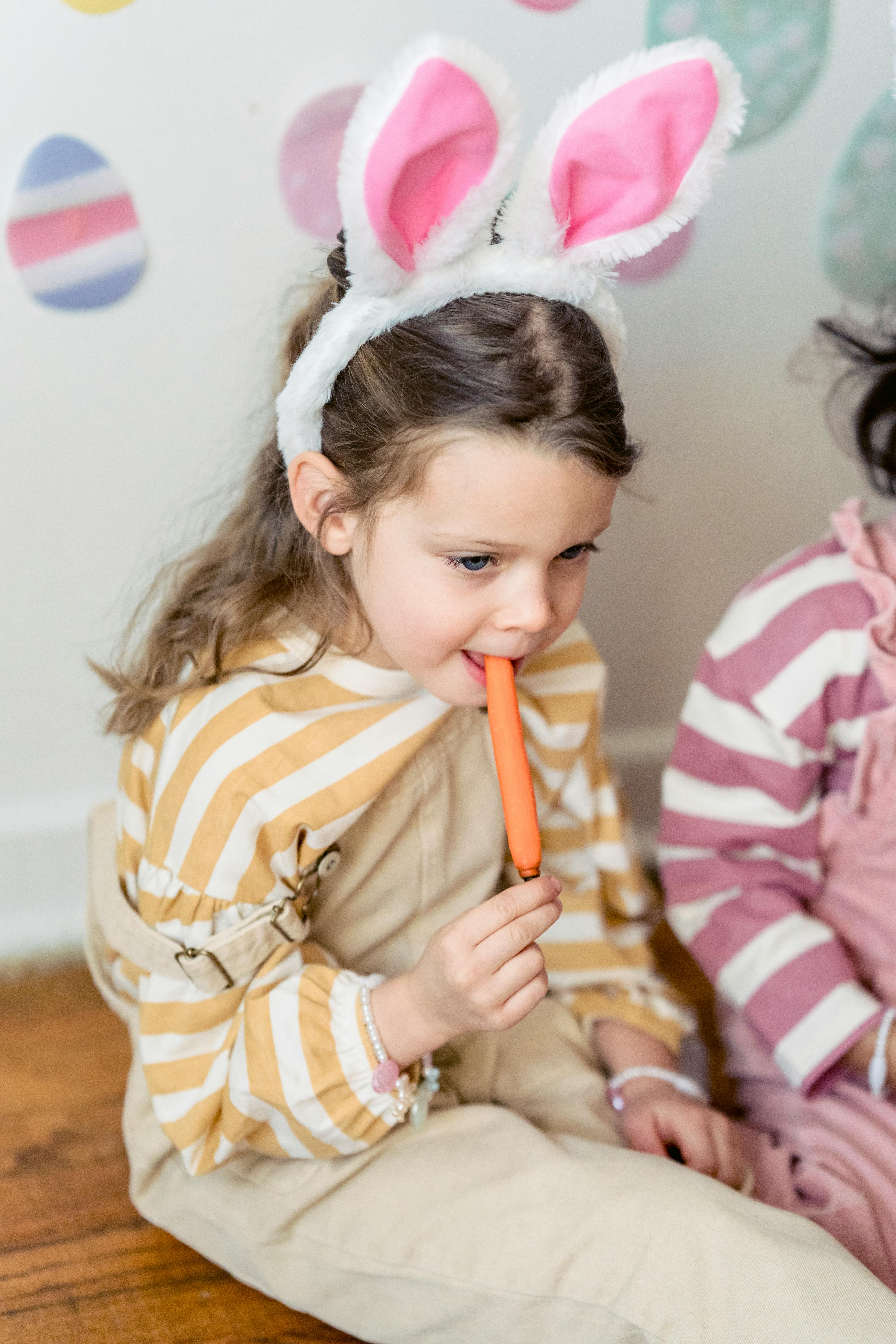 girl with bunny ears eating carrot against crop friend indoors