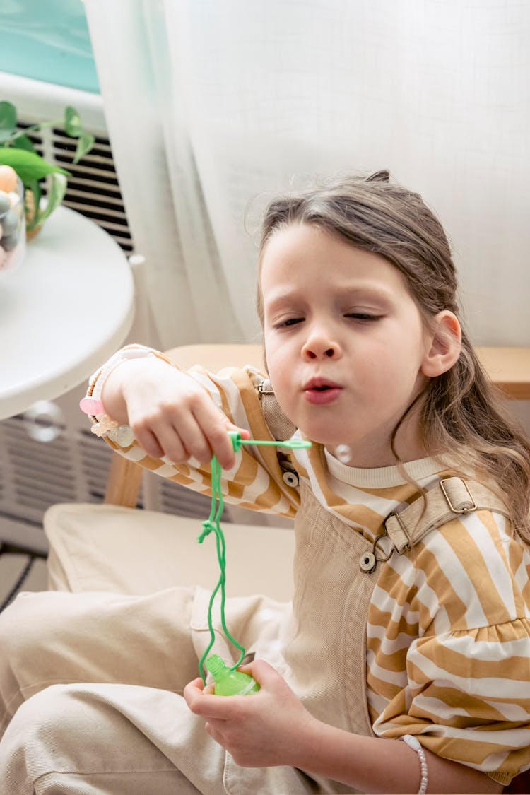 Girl Blowing Soap Bubbles In Armchair At Home