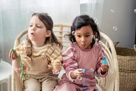 Carefree multiracial girls blowing soap bubbles in armchair at home