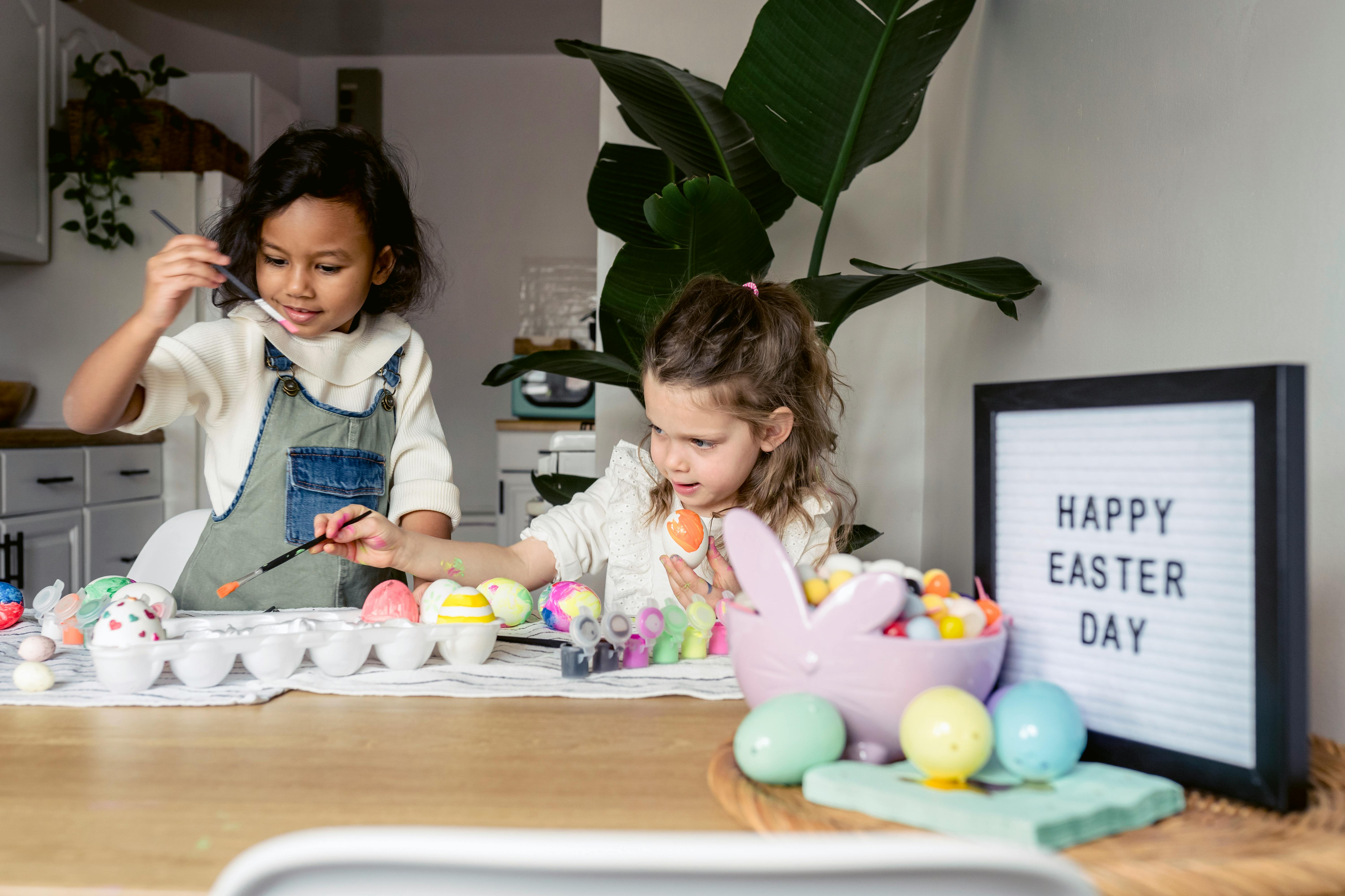 multiethnic children painting eggs on table in apartment