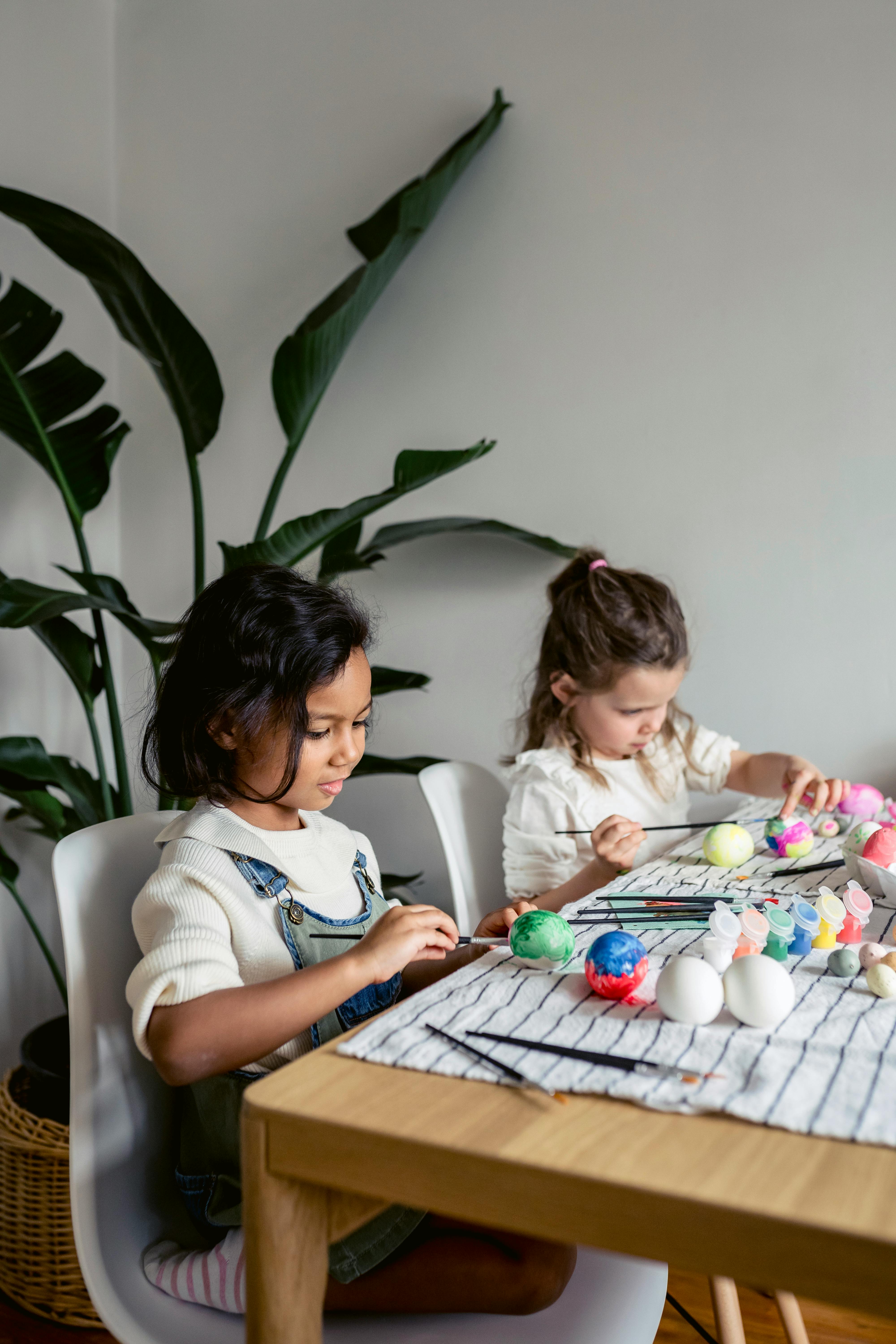 multiracial girls coloring eggs at table in home