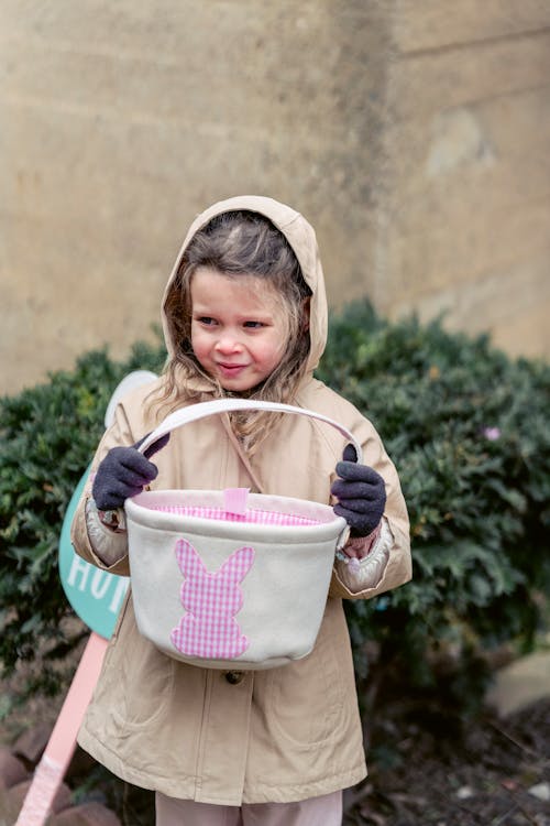 Adorable girl in coat holding textile basket for egg hunt