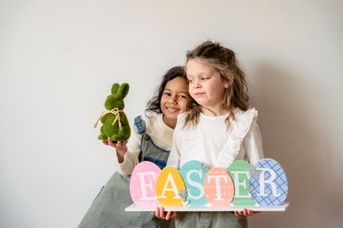 Free Cheerful Indian girl with green Easter bunny looking at camera while hugging female friend with multicolored souvenir Stock Photo