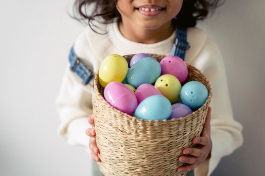 Unrecognizable little child in casual clothes standing with colorful plastic Easter eggs in wicker basket