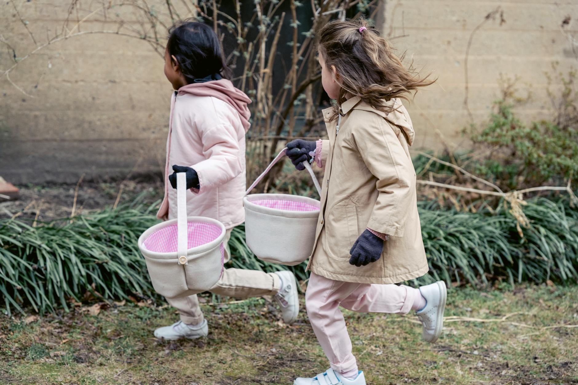 Side view of little multiracial children in warm coats with toy buckets running outside