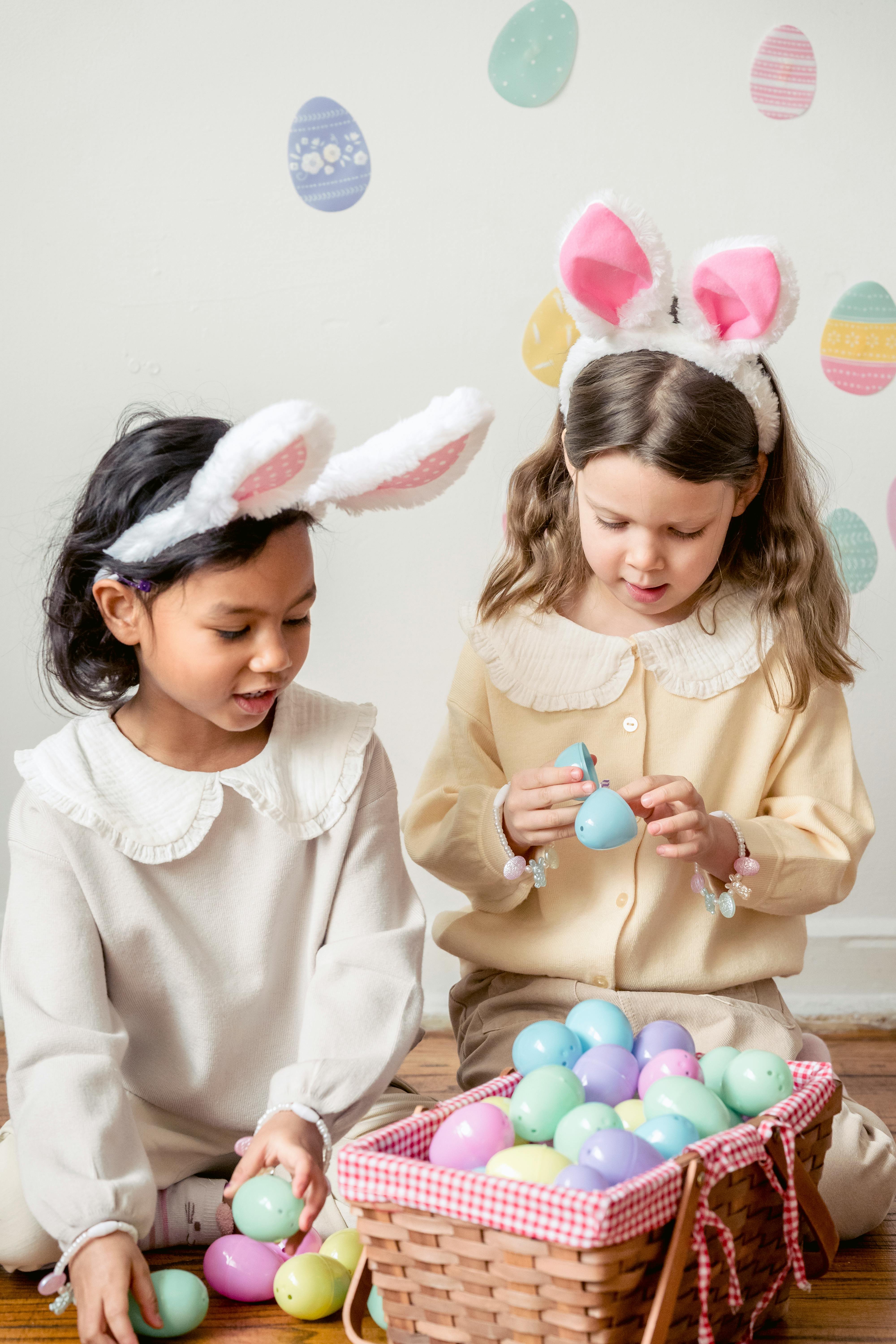 cute diverse girls in bunny ears on heads sitting near easter eggs