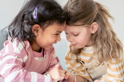 Cute multiethnic preschooler girls making gesture with fingers as sign of friendship forever while playing together in kindergarten