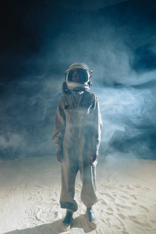 Free Person in Gray Space Suit Standing on White Sand with Smoke on Background Stock Photo