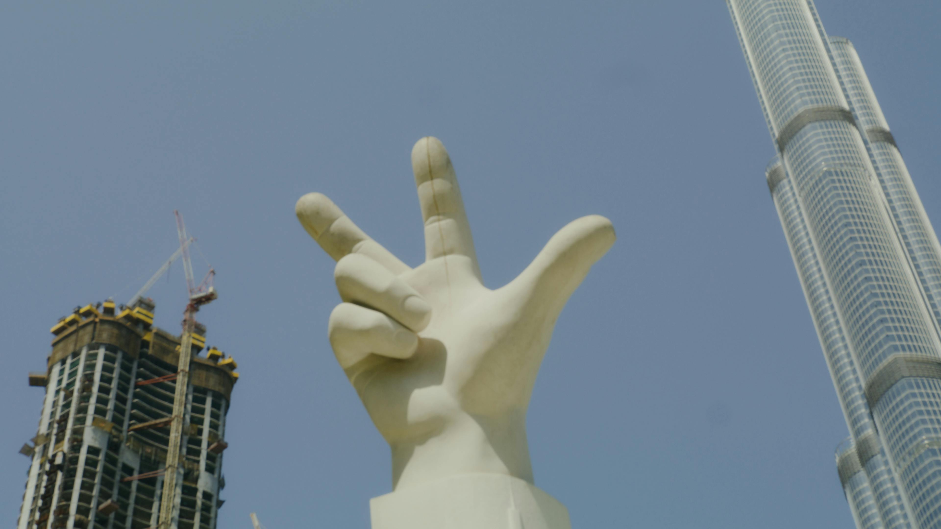 statue of a hand with three finger salute between buildings under blue sky