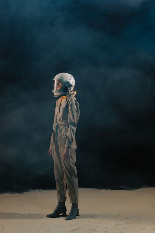 Free A person in a spacesuit stands on a sandy surface with a smoky dark background. Stock Photo