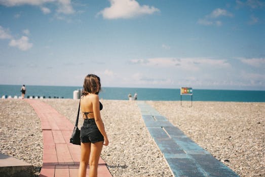 A woman standing on a pebble beach with pathways, overlooking the sea in Batumi, Georgia.