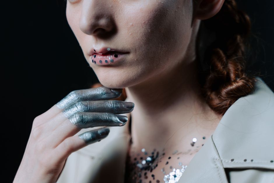 Close-up of a young woman with space-themed makeup and silver accents in a artistic pose.