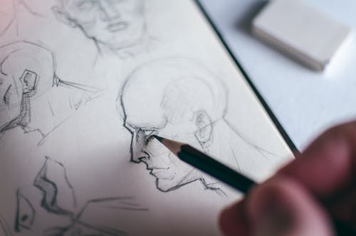 Person Sketching Human Head with a Pencil on White Paper
