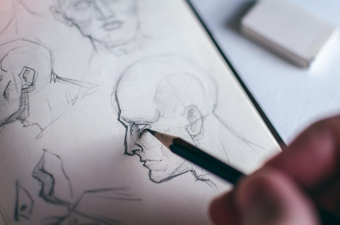 Free Person Sketching Human Head with a Pencil on White Paper Stock Photo