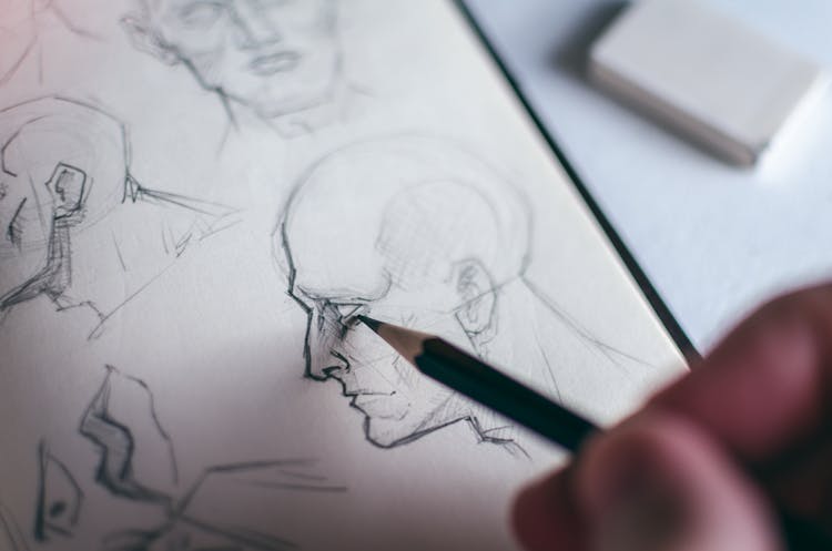 Person Sketching Human Head With A Pencil On White Paper