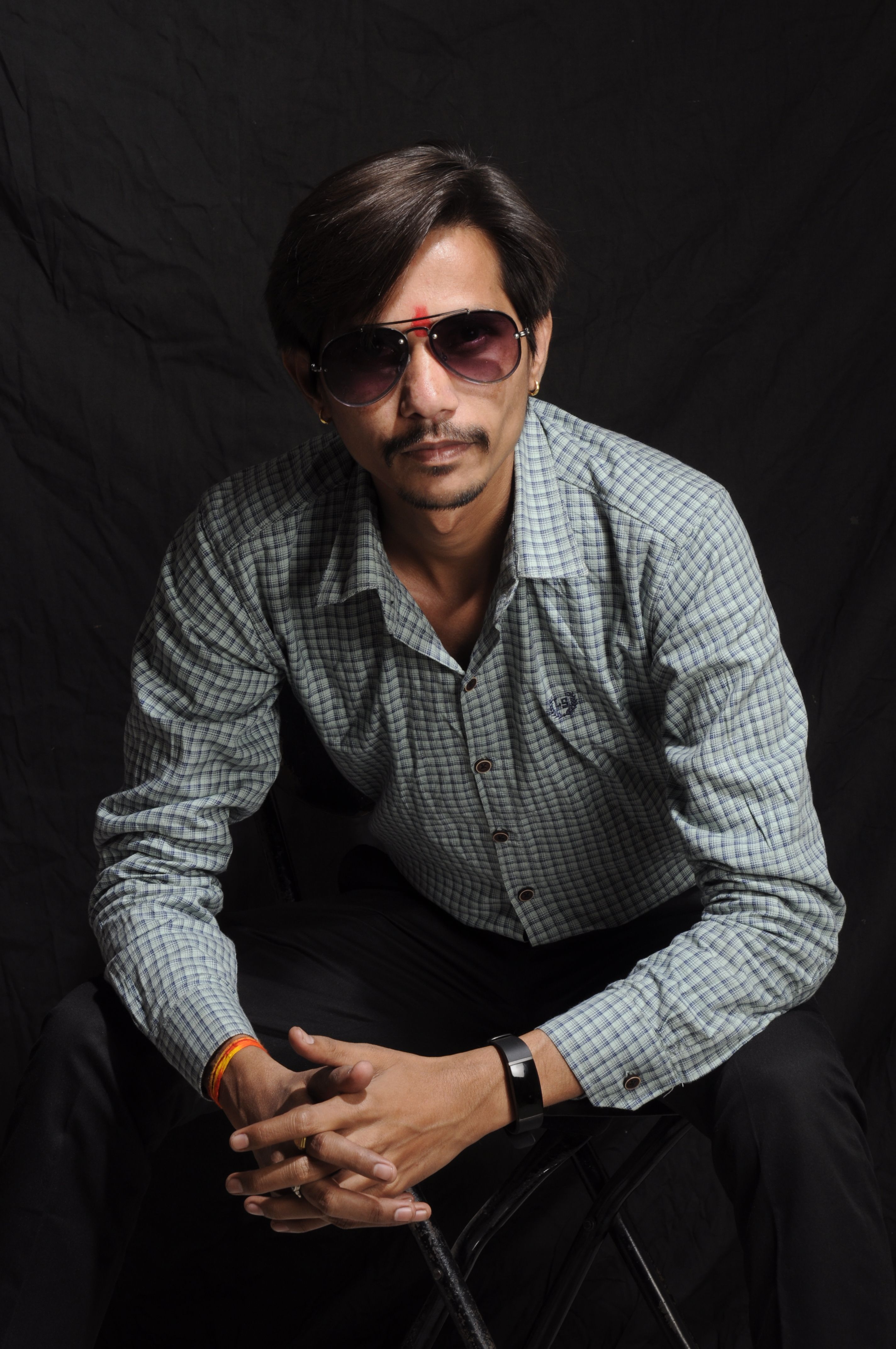 Confident man wearing sunglasses posing in studio against dark background.