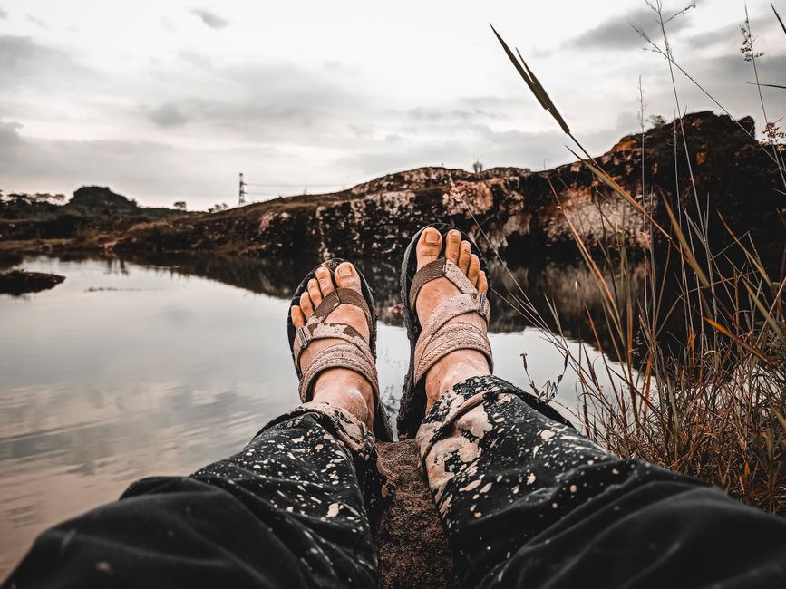 A person sitting by a tranquil lake with muddy feet, enjoying nature's serene beauty.