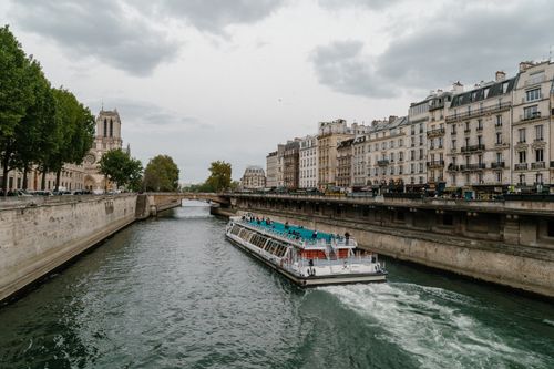 Free Boat cruising on the Seine River in Paris near Notre Dame Cathedral under cloudy sky. Stock Photo