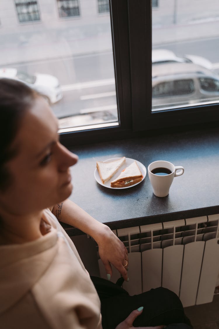 A Woman Sitting Near A Plate With A Sandwich