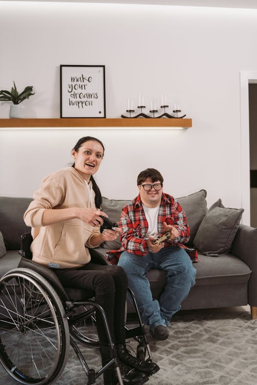 Woman in Wheelchair Playing Video Game Beside a Young Man Sitting on Couch