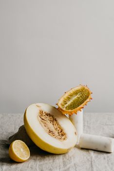 Elegant still life of sliced kiwano, melon, and lemon on textured surface.