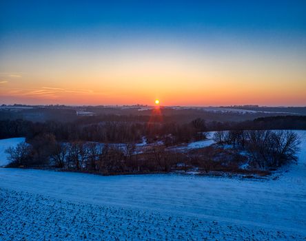 A serene winter sunset over snow-covered fields in Plainview, Minnesota, showcasing vibrant colors.