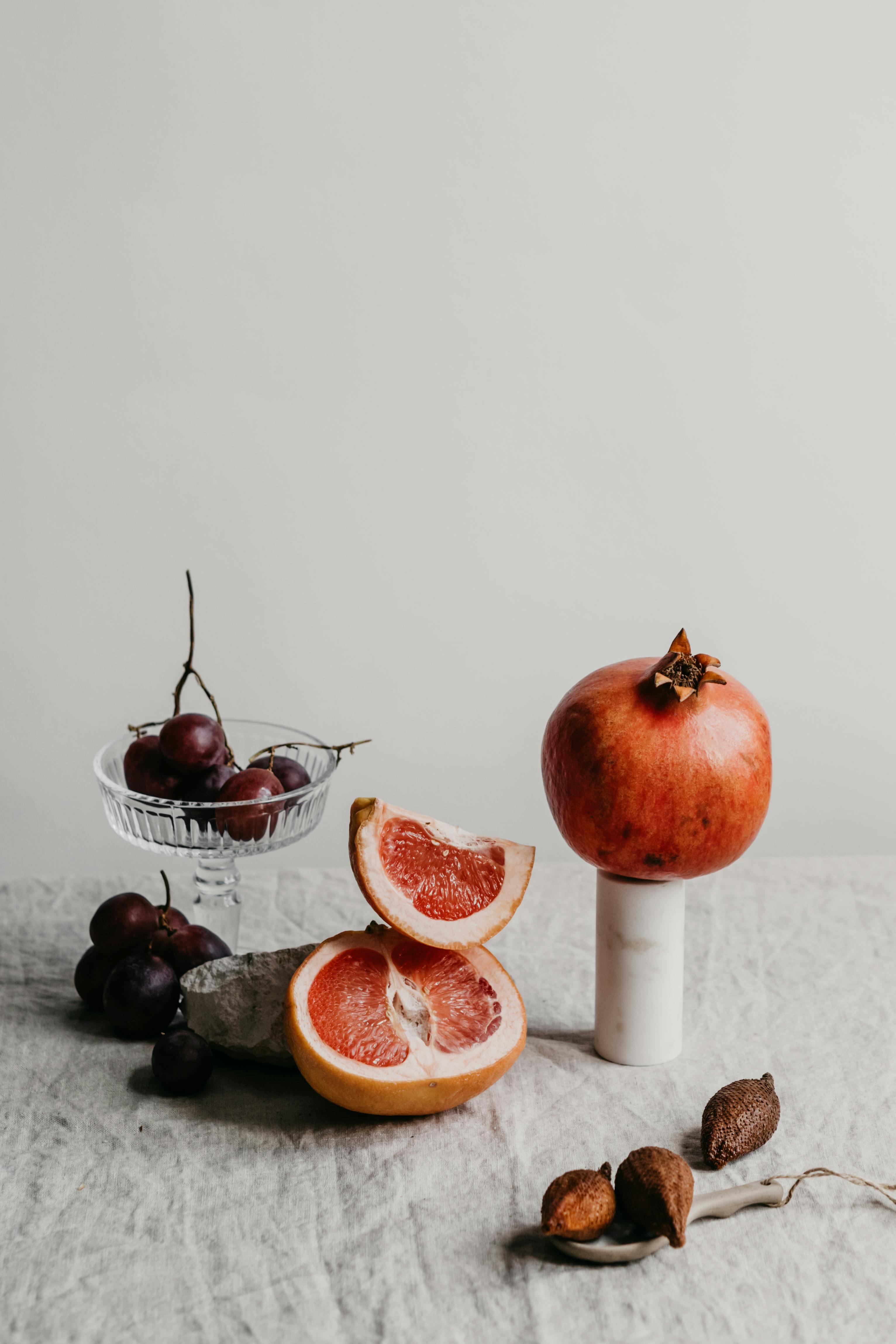 Stylish still life of fresh fruits including pomegranate, grapefruit, and grapes displayed on a textured surface.