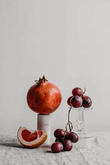 Minimalist still life featuring pomegranate, grapes, and grapefruit slice on neutral background.