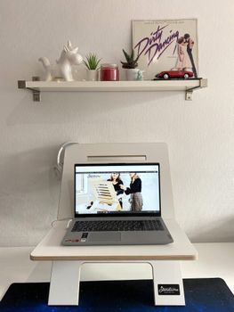 Modern home office featuring a laptop on a stand with decorative shelf above in a well-lit room.