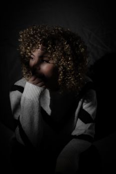 A woman with curly hair poses thoughtfully in low key lighting emphasizing shadows.. woman, with, curly