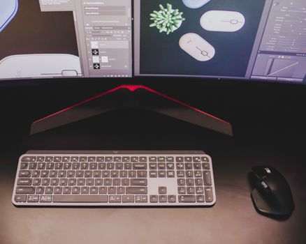 Close-up of a stylish workspace featuring a keyboard and mouse with dual monitors displaying design software.