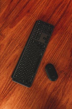 Top view of wireless keyboard and computer mouse placed on wooden table for work