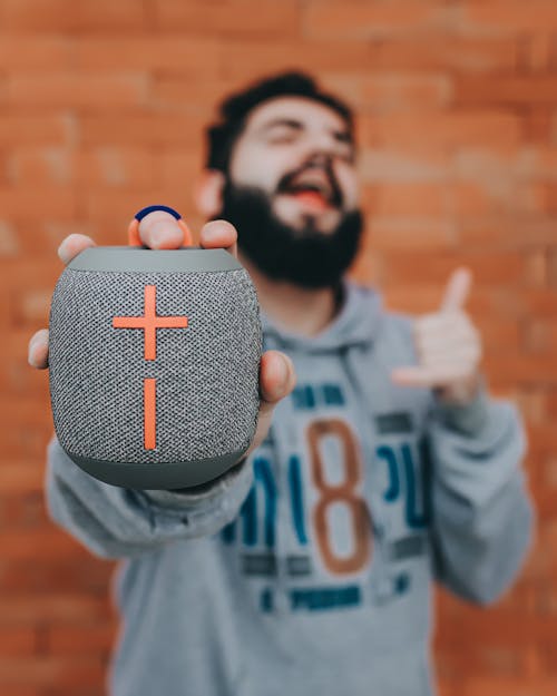 Soft focus of portable speaker in hand of bearded man singing song while listening to music