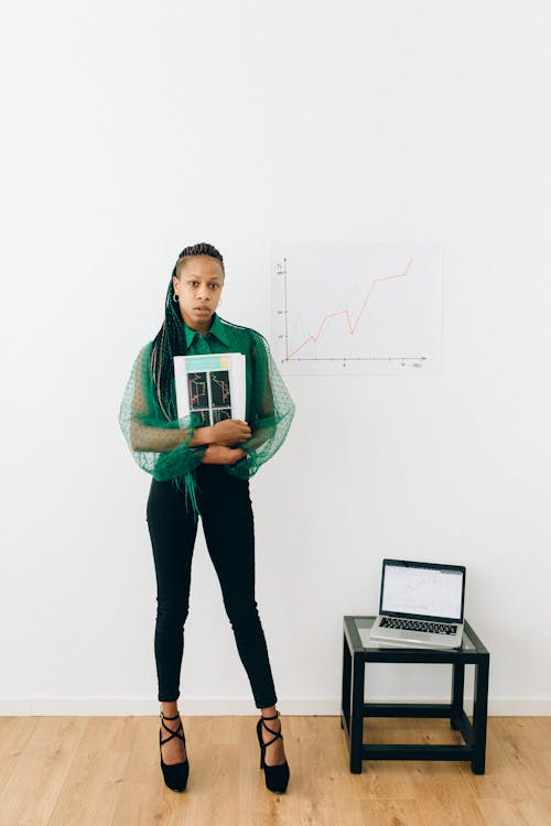 Woman Holding Pieces of Paper Near a Laptop