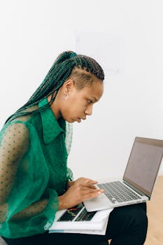 African American woman focused on remote work using a laptop in a bright indoor space.